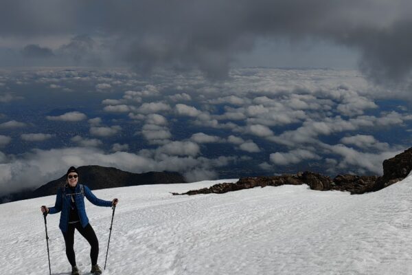 A hiker enjoys the snowy slopes of Cerro Provincia, with Santiago visible through the clouds below.