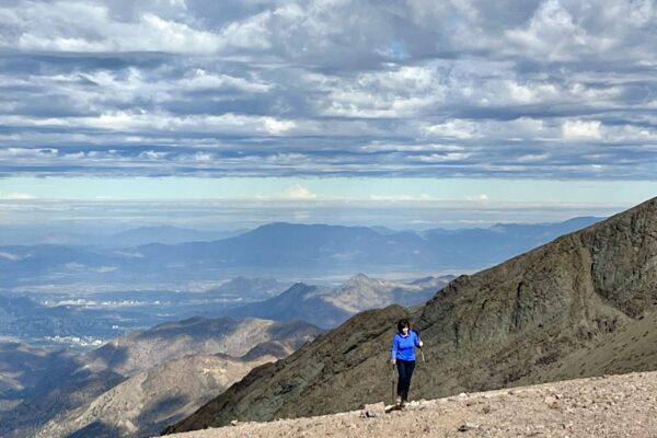 A hiker climbs a rocky trail toward the summit of El Pintor, with Santiago spread across the valley far below.